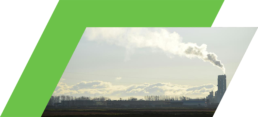 A factory emits smoke against a backdrop of a clear sky and distant clouds.