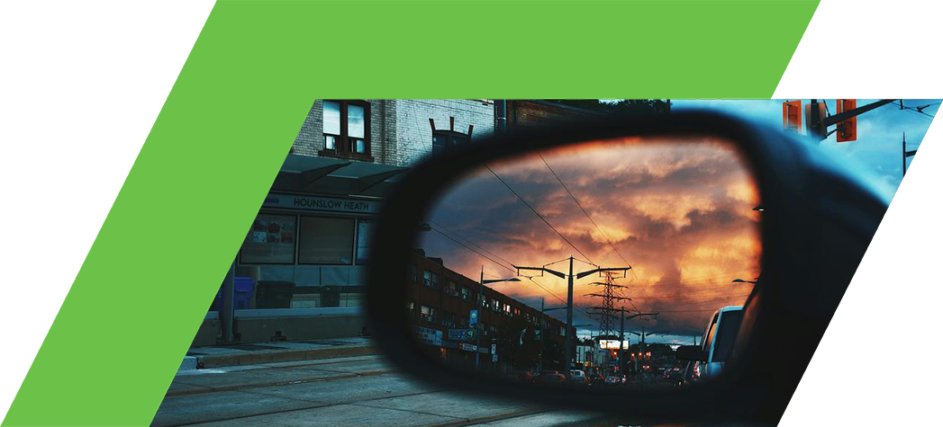 A side mirror reflects a vibrant sunset over a city street, capturing buildings and power lines.