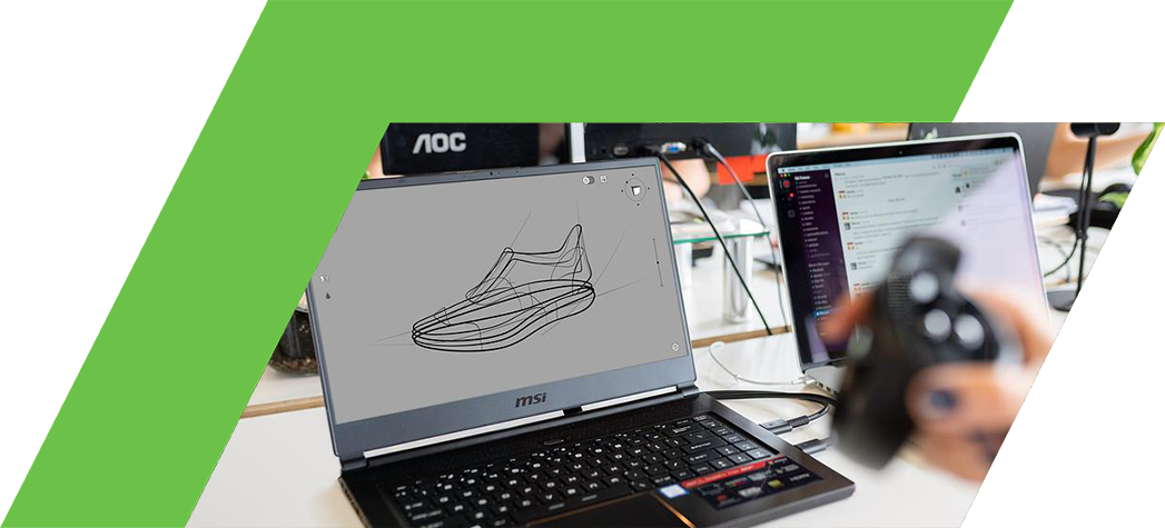 A person holds a controller while working on a laptop displaying a sketch of a shoe in a modern office environment.