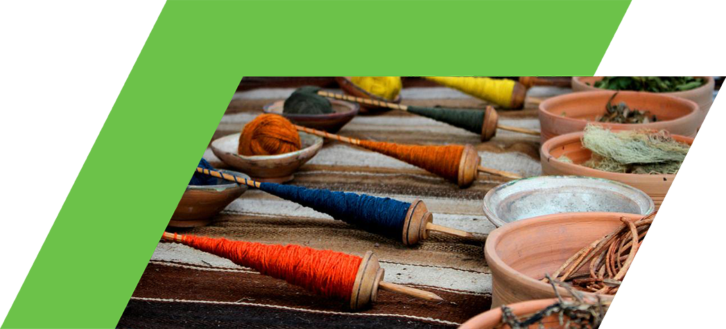 Colorful spindles and bowls filled with natural fibers and herbs displayed on a woven textile surface.