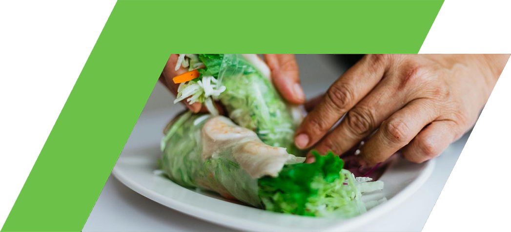 A person is preparing fresh spring rolls filled with vegetables and shrimp on a white plate.