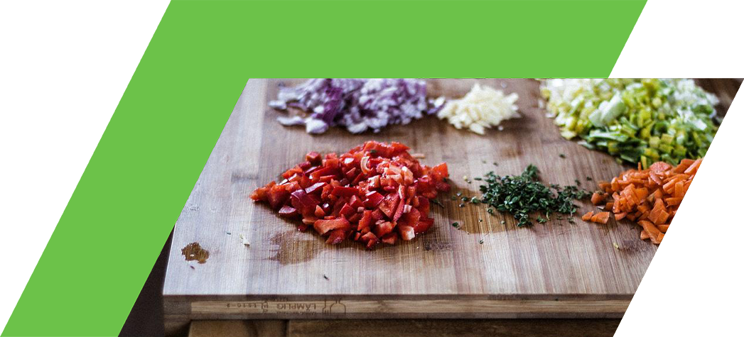 Chopped vegetables including red bell pepper, onion, garlic, green onion, carrot, and thyme arranged on a wooden cutting board with a knife.