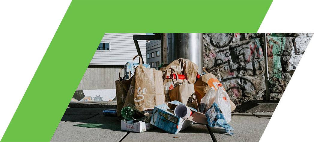 A pile of discarded bags and trash lies on the ground near a stone wall and a trash can.