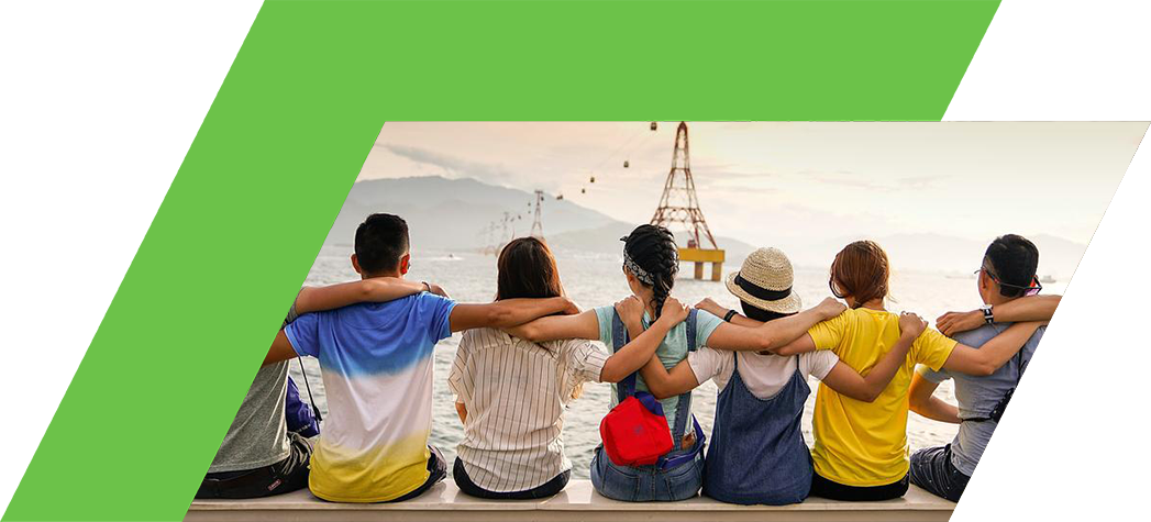 A group of friends sitting together on a ledge, enjoying a scenic view of the ocean and mountains.