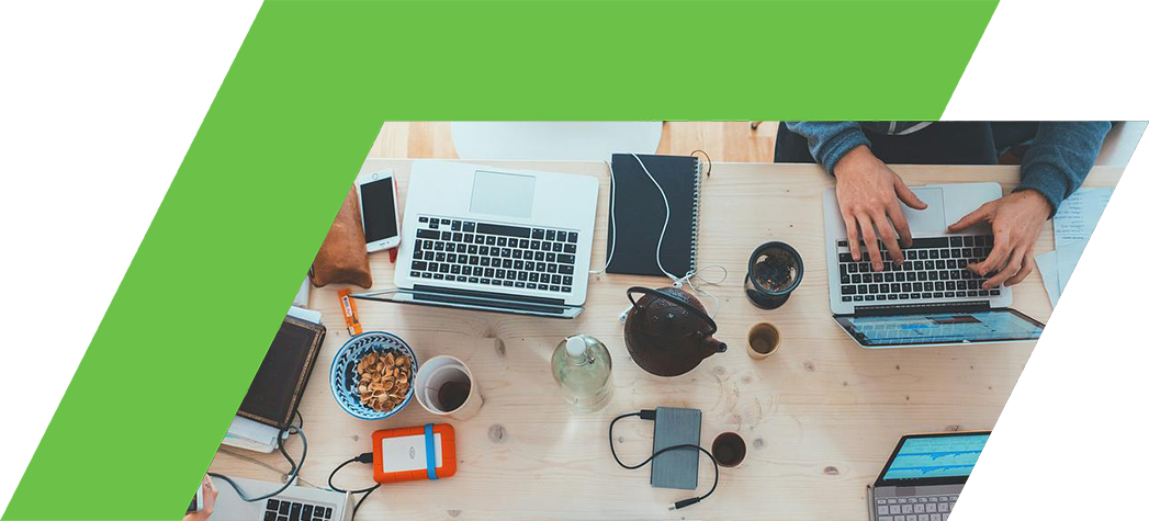 Aerial view of a collaborative workspace with multiple laptops, notebooks, and personal items on a wooden table.