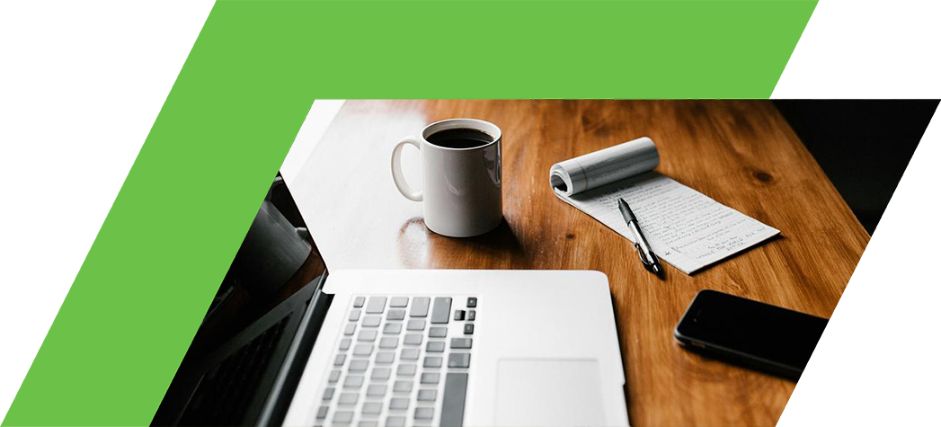 A laptop, a coffee mug, a notepad, and a smartphone are arranged on a wooden table near a window.