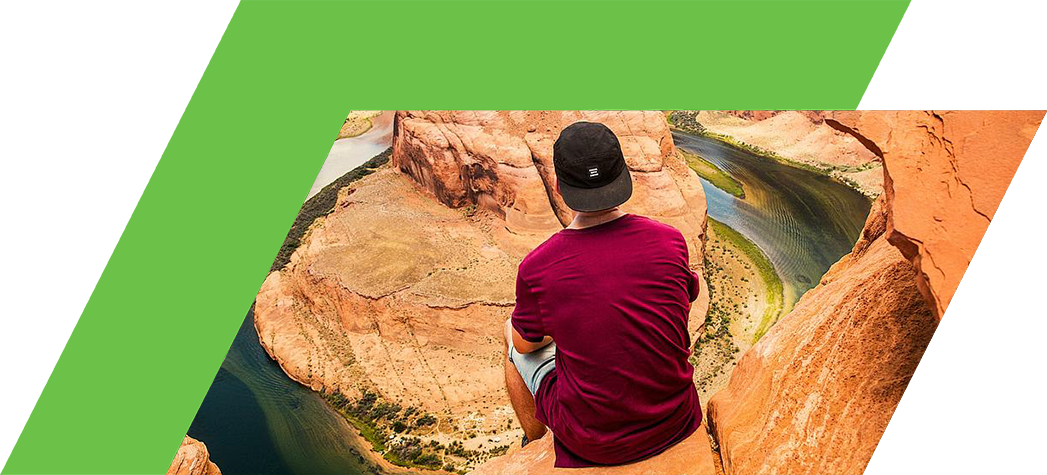 A person sits on a rock ledge overlooking a winding river and canyon landscape.