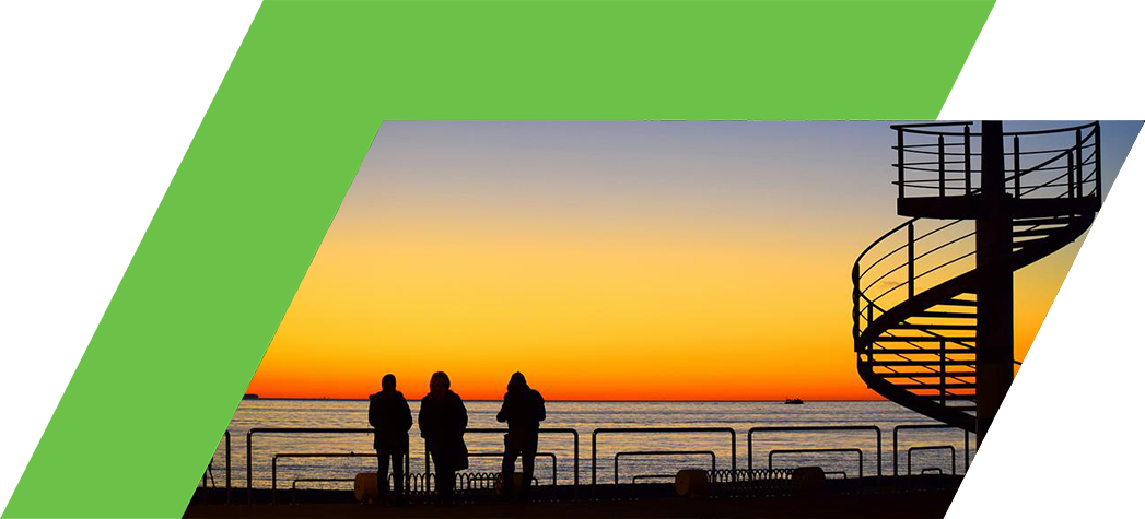 Silhouettes of three people standing by the water at sunset, with a spiral staircase in the foreground.