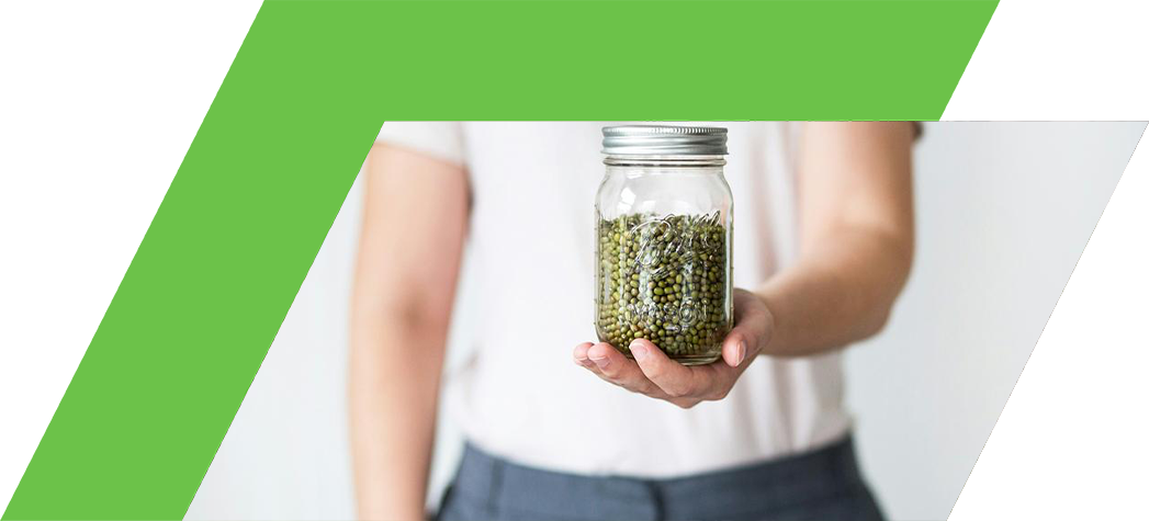A person holds a glass jar filled with green lentils against a light background.