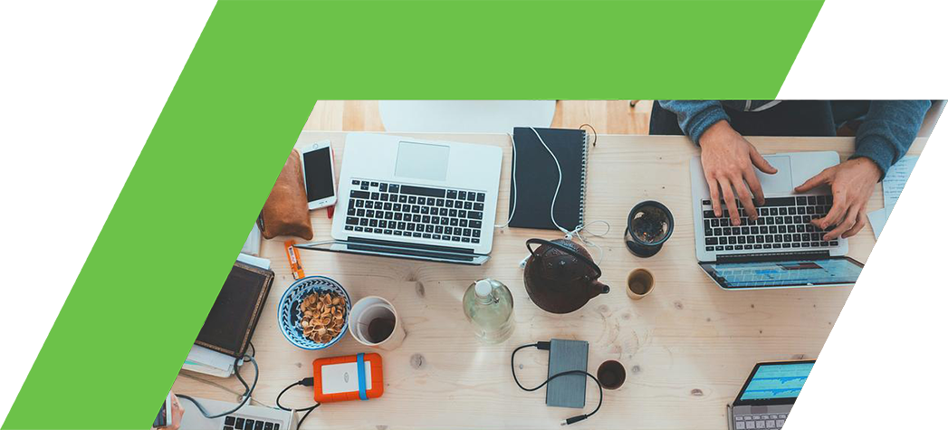 Aerial view of a collaborative workspace with multiple laptops, notebooks, and various personal items scattered on a wooden table.