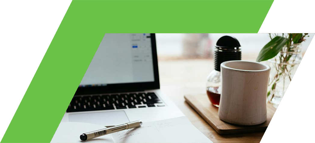 A laptop, an open notebook with a pen, a coffee cup, and a vase with flowers on a wooden table.