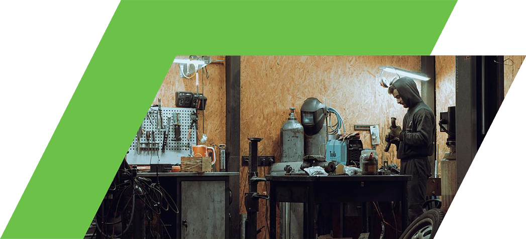 A mechanic working in a dimly lit garage filled with tools and equipment.