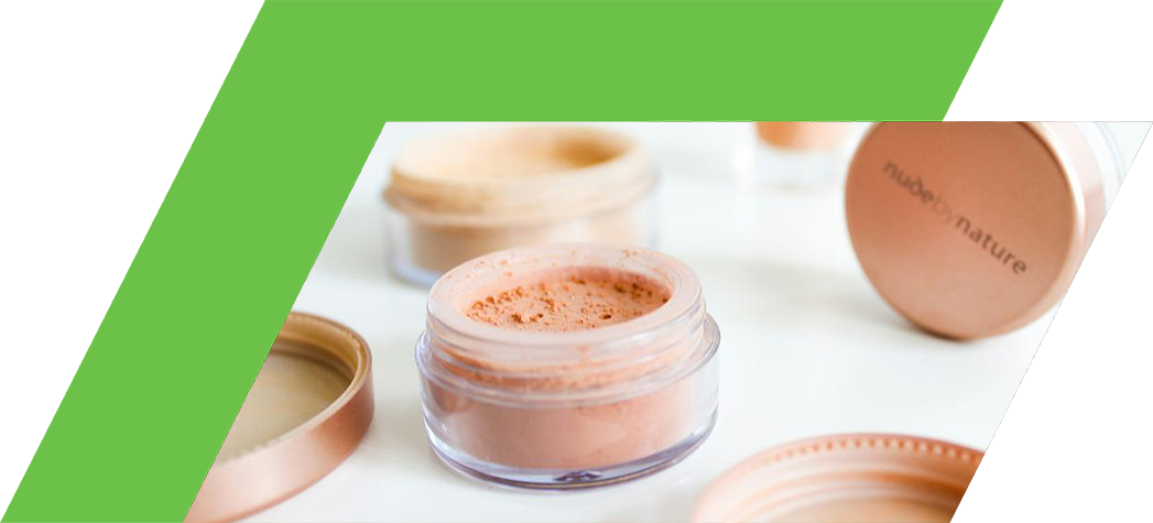 Various jars of loose powder makeup from the brand Nude by Nature are displayed on a white surface.