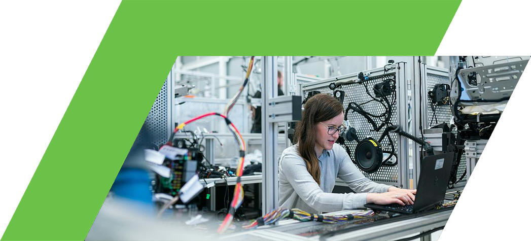 A woman working on a laptop amidst machinery and wiring in a modern industrial setting.