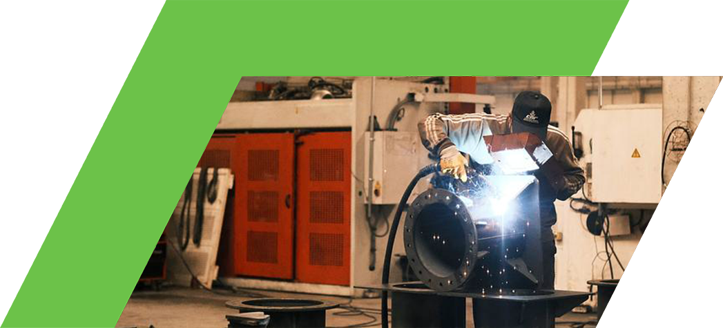A welder working on a metal piece in a factory setting, surrounded by various tools and equipment.