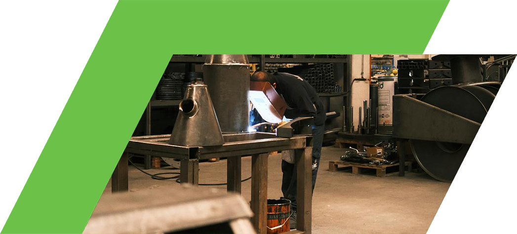 A worker is welding metal components in a workshop filled with various tools and materials.