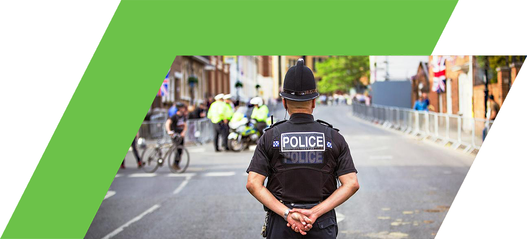 A police officer stands with hands clasped behind his back, watching over a street decorated with Union Jack flags.