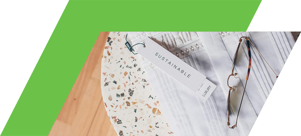 A neatly folded white garment with a "SUSTAINABLE" tag sits beside a pair of stylish eyeglasses on a speckled tabletop.