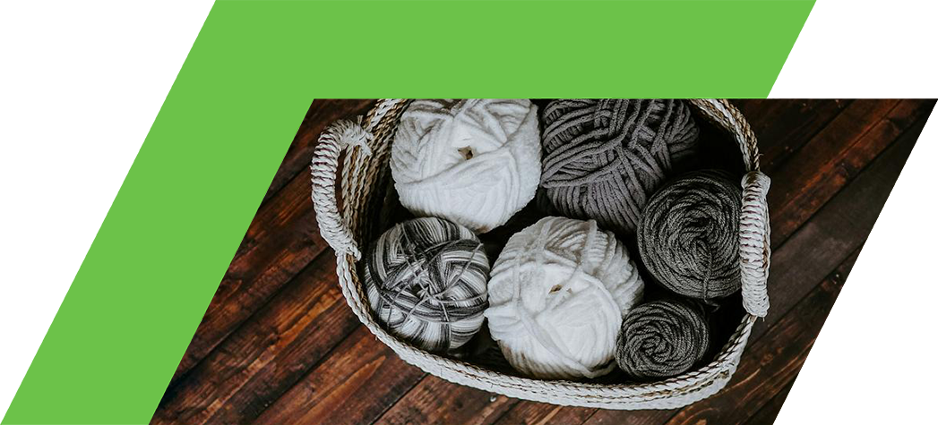 A woven basket filled with various balls of cream and gray yarn on a wooden surface.