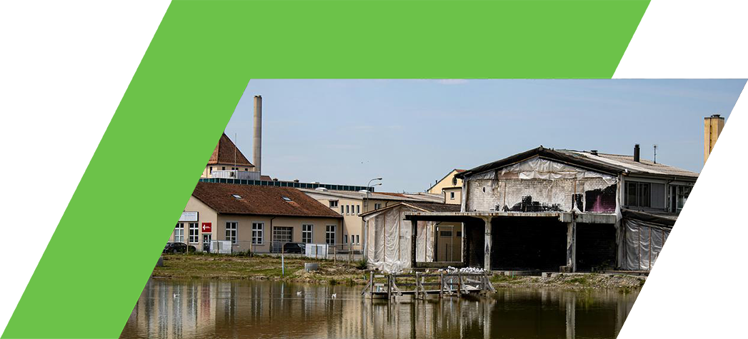 A partially demolished building with a reflective water surface in the foreground, surrounded by industrial structures and a clear sky.