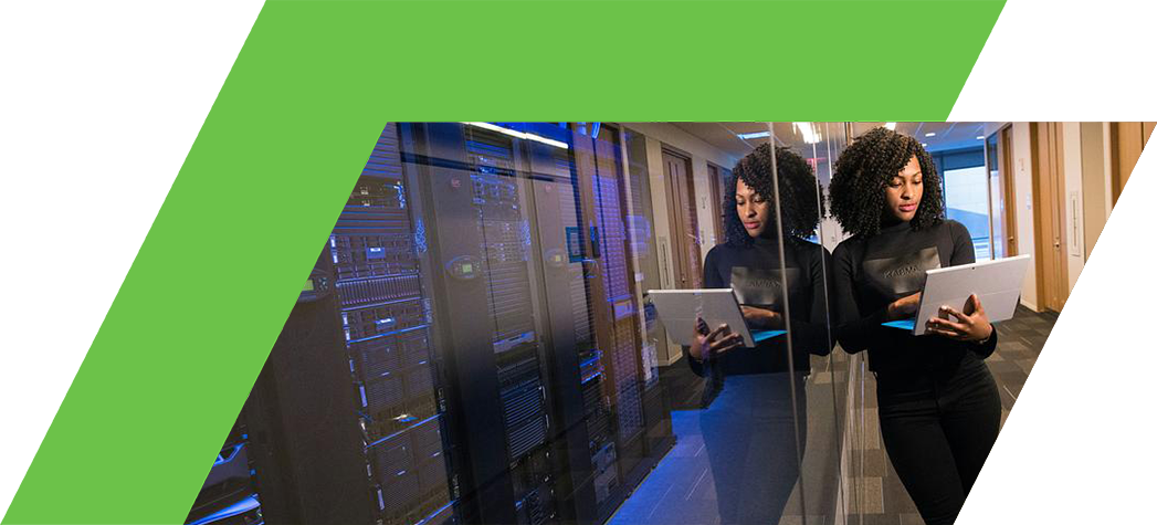 A woman stands in a modern data center, holding a laptop and reflecting on a glass wall alongside rows of server racks.