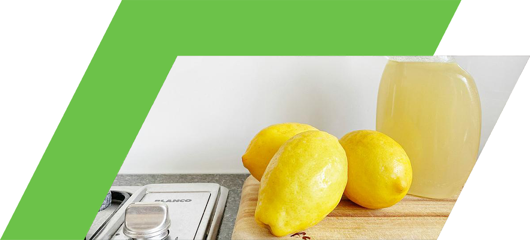 A spray bottle filled with lemon juice sits next to three fresh lemons on a wooden cutting board.