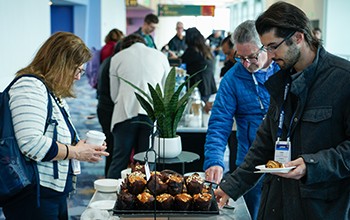 Several individuals stand around a table laden with food, sharing a meal and socializing in a lively atmosphere.